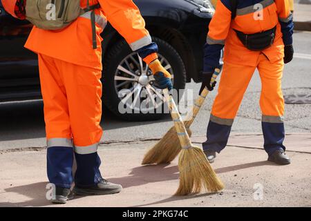 Two janitors in orange uniform sweeping the street on car background. Cleaning spring city Stock Photo