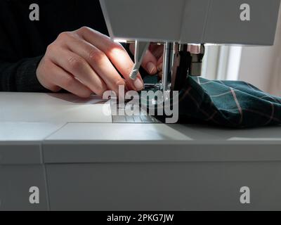 Woman sews a piece of clothing on a modern electric sewing machine. Close up image. Stock Photo