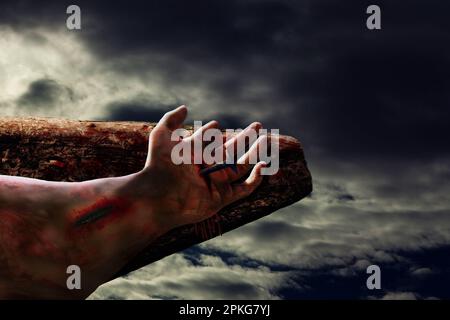 Dramatic scene of Jesus crucifixion showing hand of Christ with blood and bruise nailed to wooden cross symbolic of Christian Easter and Good Friday Stock Photo