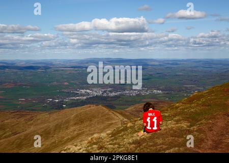 UK Weather: Good Friday bank holiday, April 7th, 2023. Brecon Beacons National Park, South Wales. A boy wearing a Gareth Bale #11 Wales football shirt plays with his smartphone on the summit of Pen y Fan in the Brecon Beacons National Park. The town of Brecon is in the distance. Beautiful sunny weather meant many people made the trip to the Park for today's bank holiday. Stock Photo
