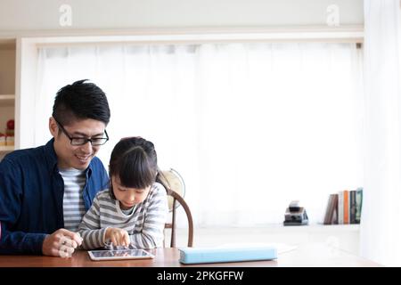 A girl using a tablet and her father helping her Stock Photo