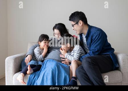 Sisters and father talking to pregnant mother's belly Stock Photo