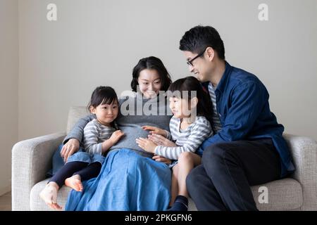 Little sister and father putting their hands on pregnant mother's stomach Stock Photo