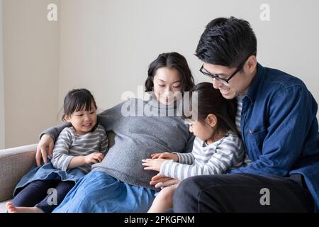 Little sister and father putting their hands on pregnant mother's belly Stock Photo