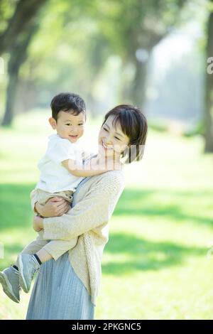 A mother holding and smiling at her child in a row of poplar trees Stock Photo
