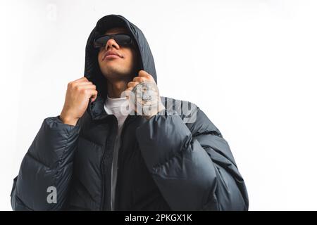 young tattooed man with sunglasses touching his winter jacket, isolated studio shot medium. High quality photo Stock Photo
