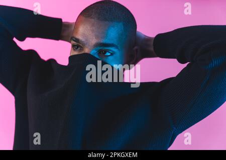 Unrecognisable incognito male model with face covered by his black hoodie over pink background. Face covering concept. High quality photo Stock Photo
