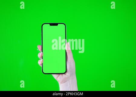 Child hand touching clicking on mobile phone with chromakey screen. Little Baby Finger Taps in center of blank phone green display. Close up. Using smartphone device. Top view Flat lay. Stock Photo