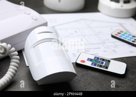 Movement detector, intercom, remote controls and building plan on grey table, closeup. Home security system Stock Photo
