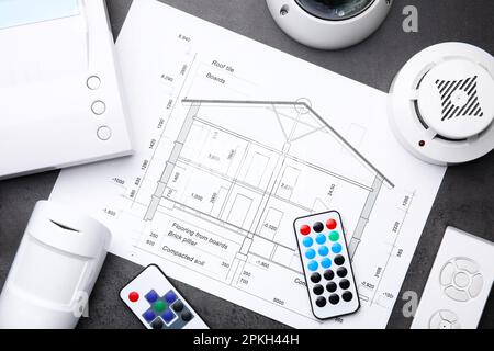 Building plan, remote controls, smoke and movement detectors on grey table, flat lay. Home security system Stock Photo
