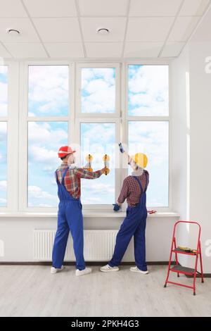 Workers using suction lifters during plastic window installation indoors Stock Photo