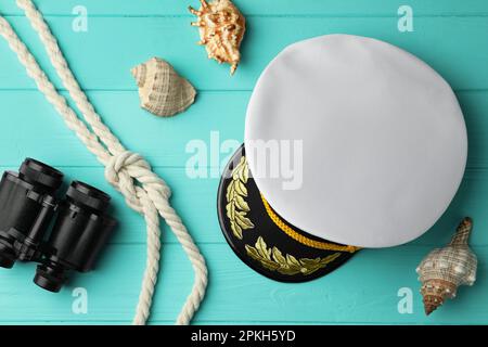 Peaked cap, rope, shells and binoculars on turquoise wooden background, flat lay Stock Photo