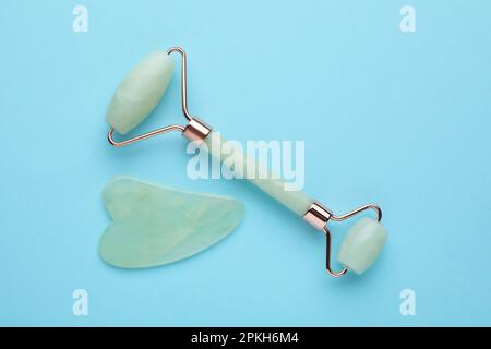 Jade gua sha tool and facial roller on light blue background, flat lay Stock Photo