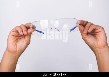 Hand holding safety glasses, personal protective equipment. Protective glasses in hand isolated on white background. Stock Photo