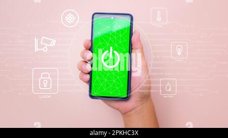 Male hand holding smart phone on pink background with smart home technology interface on smartphone app screen. Concept of automation. Stock Photo