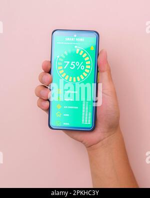 Male hand holding smart phone on pink background with smart home technology interface on smartphone app screen. Concept of automation. Stock Photo