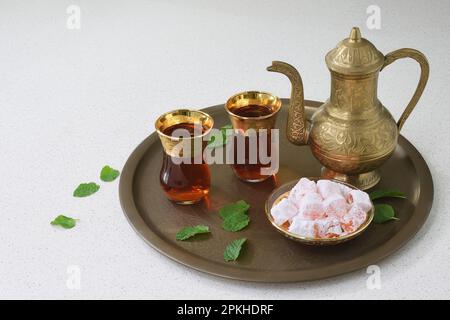A classic, celebratory, ornate Turkish teapot, two glasses and traditional turkish delights on a tray in soft lighting with copy space to the left Stock Photo