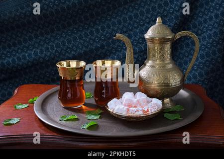 A classic, celebratory, ornate Turkish teapot, two glasses and traditional turkish delights on a tray and wooden table in soft mood lighting Stock Photo