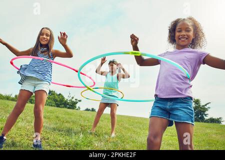 Its hard not to be happy when youre hula hooping. a group of young girls playing with hula hoops in the park. Stock Photo