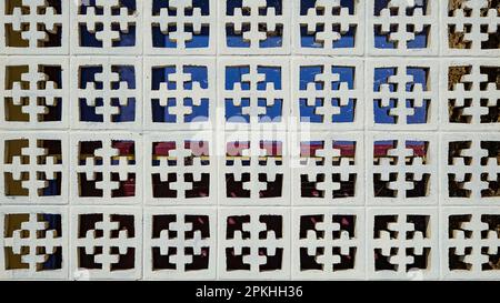 Geometric pattern in a wall of white concrete blocks with blue, red and yellow colours in the background Stock Photo