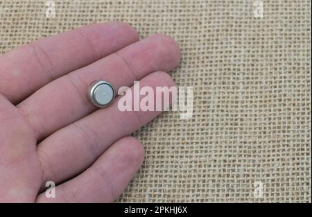 Man's hand holding a LR44 battery on a sackcloth background, close up Stock Photo