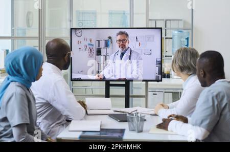 Mature doctor on the screen having video call with his colleagues during online meeting in office Stock Photo