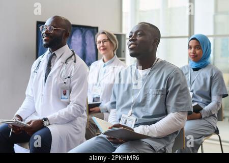 Group of doctors making notes during medical conference, they sitting on chairs and listening to speaker Stock Photo