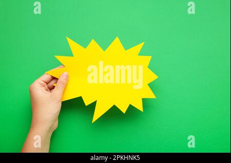 Hand holding an yellow speech bubble on green background. Top view Stock Photo