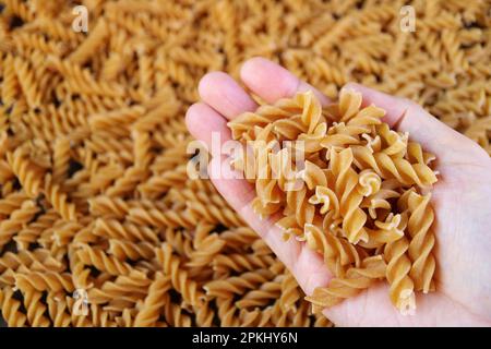 Heap of Dried Whole Wheat Fusilli Pasta in Hand with Blurry Pasta in Background Stock Photo