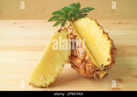 Piece of fresh ripe pineapple cut from the whole fruit isolated on wooden table Stock Photo