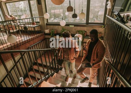 Three multiracial people walking upstairs at the coffee bar and talking business. They are about to work remotely Stock Photo