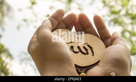 Arabic 'Allah' written in English meaning of God. Muslim woman hands holding heart shaped tag Stock Photo