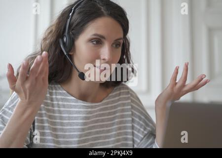 Confident focused young spanish businesswoman wearing wireless headphones having video call conversation with partner or giving professional consultat Stock Photo