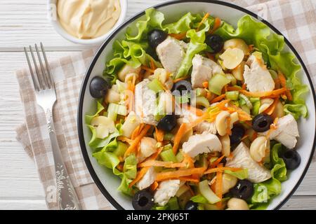 Healthy diet salad with chicken, mushrooms, carrots, celery, olives, cheese and lettuce close-up in a bowl on a wooden table. Horizontal top view from Stock Photo