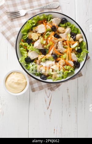 Italian Piedmontese salad with chicken, mushrooms, carrots, celery, olives, cheese and lettuce close-up in a bowl on a wooden table. Vertical top view Stock Photo