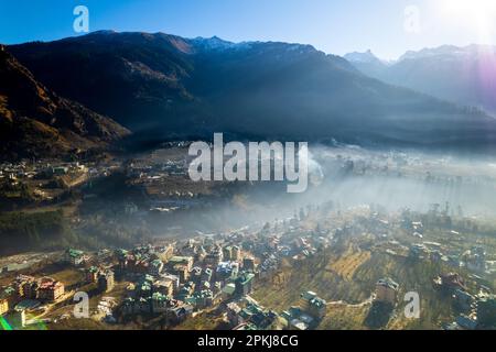 aerial drone shot gaining height over fog covered valley town of manali hill station with himalaya range in distance showing this popular tourist Stock Photo