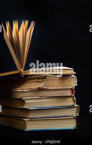 Stack of hardcover old books with an open book on a dark background. Bookshelf shop, Knowledge publications, literature. Bookish bookstore bookstore. Stock Photo