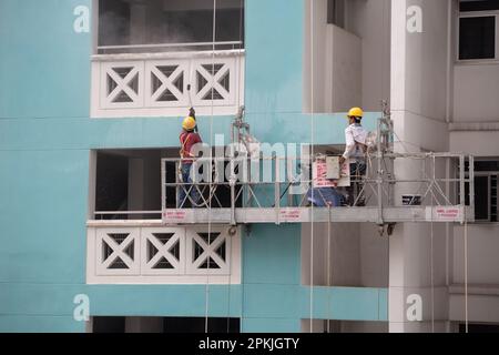 Two workers on scaffold elevator, one working using water jet to clean off dirt of the wall exterior and the other control the height elevation. Stock Photo