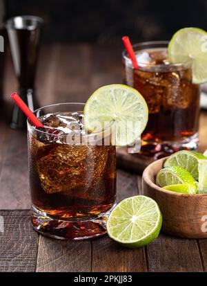 Rum and cola cocktail with lime slice on rustic wooden table Stock Photo