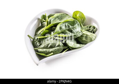 Heart-shaped bowl of young spinach leaves on an isolated white background. Stock Photo