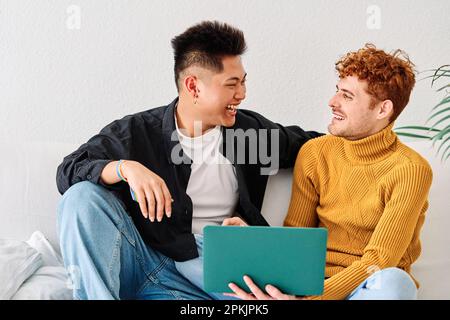 Multiethnic gay couple using a laptop sitting in the sofa Stock Photo