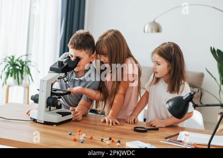 Using microscope. Kids having fun in the domestic room at daytime together Stock Photo