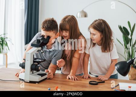 Using microscope. Kids having fun in the domestic room at daytime together Stock Photo