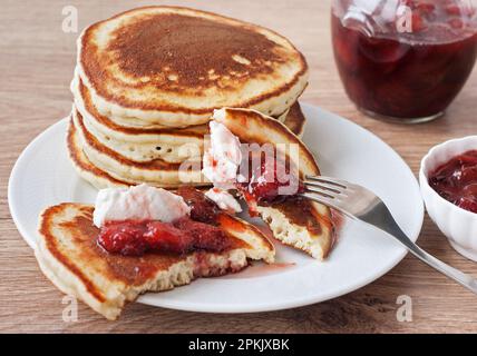 A stack of delicious sweet and spicy American pancakes with strawberry jam and sour cream on a white plate. Breakfast Stock Photo