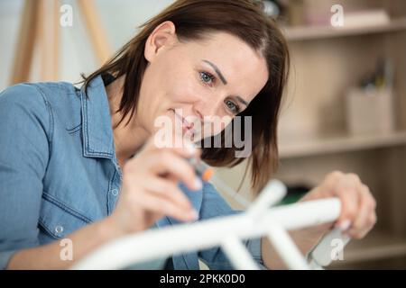 smiling woman assembling wooden furniture using screwdriver Stock Photo