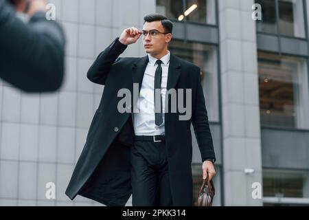 Posing for photographer. Businessman in black suit and tie is outdoors in the city Stock Photo