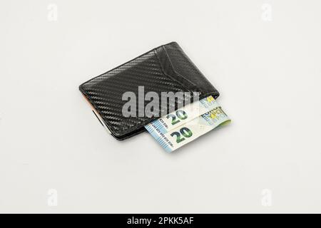 A black carbon fiber braided wallet filled with euro banknotes on a smooth white surface Stock Photo