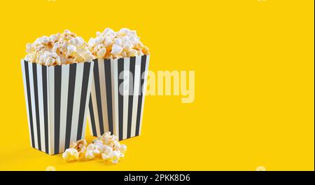 Two black white striped carton buckets with tasty cheese popcorn, isolated on yellow background. Box with scattering of popcorn grains. Fast food, mov Stock Photo