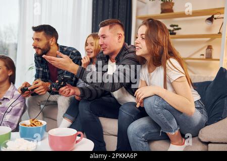 Playing video game. Group of friends have party indoors together. Stock Photo