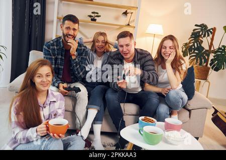 Playing video game. Group of friends have party indoors together. Stock Photo